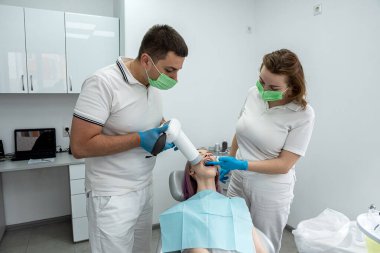 Genç erkek dişçi, dişçi muayenehanesinde dişçi asistanıyla dişlerinin fotoğrafını çekiyor. Diş sağlığı ve diş bakımı.