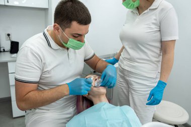 Erkek dişçi bir hastanın dişlerini tedavi eder ve kadın asistan ona yardım eder. Sağlıklı ağız boşluğu. dişçilik