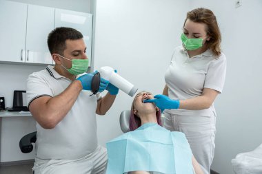 male dentist is photographing the teeth of a girl patient next to a female assistant. The concept of a dental clinic