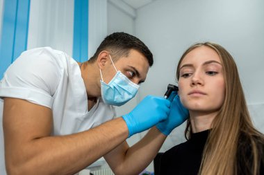 Bir otolaryngolog başakçığı inceliyor. Duyma kliniği. Maskeli ve eldivenli bir KBB doktoru hastanın kulağını muayene eder..