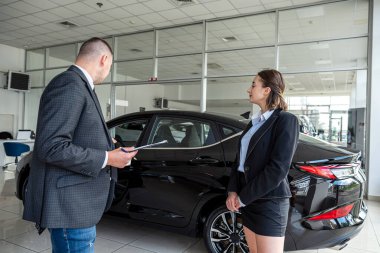 Erkek menajer modern araba galerisinde kadın müşteriye hayallerindeki arabayı seçmesinde yardım eder.