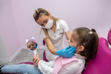 little female patient in the dental chair looks at her teeth after their treatment. dental office. mirror in hands