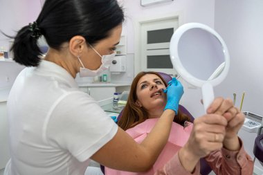 dentist examines a girl patient who holds a mirror to see everything. examination and consultation of a beautiful patient. healthy oral cavity