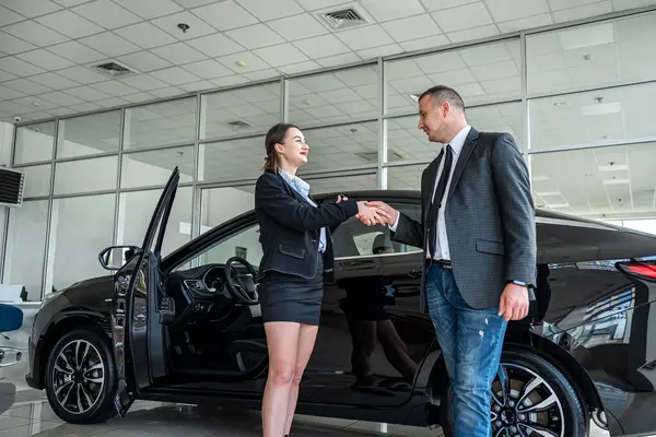 bbusiness client shaking hands with sales agent in suit after  successful deal buying a car in auto showroom
