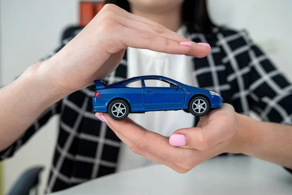 Small blue  toy car and female hand at office desk as insurance. Protection of automobile concept