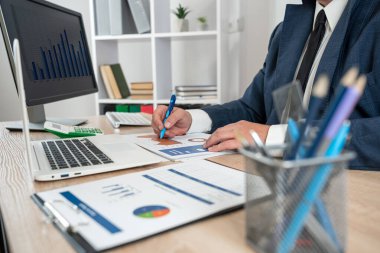 Adam takım elbise giyer şirket grafiklerini ve diyagramlarını finanse etmek için analiz eder ve beyin fırtınası yapar.