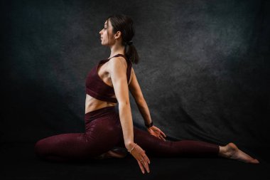 Spor kıyafetli, beyaz, çekici bir kadın stüdyonun koyu siyah arka planında yoga yapıyor. Kuvvet ve motivasyon