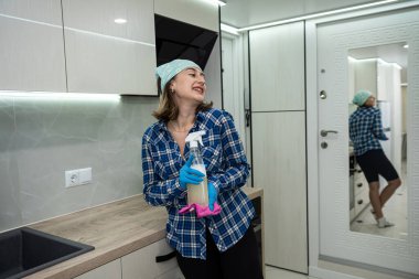 beautiful female housewife in protective gloves cleans the electric stove with a rag and a sprayer that dissolves grease. wet cleaning in the kitchen. cleanliness and order