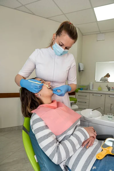 Bir dendal kliniğinde oturan güzel genç bayan diş beyazlatma için renk ve doğru diş rengini seçiyor. 