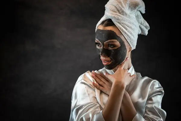 Beautiful young woman with black clay mask isolated on black. Face treatment. Spa anti aging treatment. Skin care