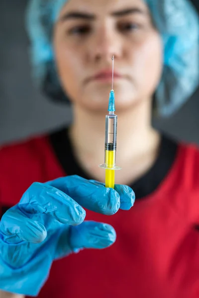 Young attractive woman doctor in blue gloves holding syringe with injection. Concept of health and science