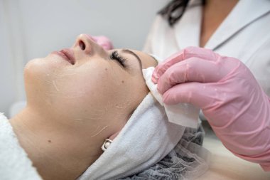 Güzellik uzmanı bir müşterinin kaplıca salonundaki yüzüne nemlendirici sürüyor ya da çıkarıyor.