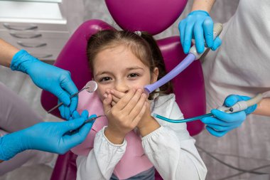 Diş hekimi, korkmuş bir çocuğu bir diş kliniğinde muayene edecek. Sevimli bebek hasta diş ağrısı çekmekten korkuyor. Ağzını panikle kaplıyor.