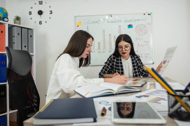 İki genç iş kadını ofiste beyin fırtınası toplantısı olarak finansal tabloları tartışıyor. İşbirliği yapın.