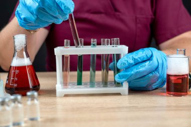 Kırmızı üniformalı ve eldivenli profesyonel bilim adamı test tüpleriyle reaktörleri karıştırıyor. Kimya bilim laboratuarı şişesi.