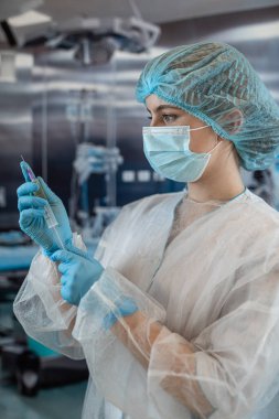 Doktor kadın anestezi uzmanı ameliyattan önce ameliyathanede bir iğne hazırlıyor. Tıbbi sağlık konsepti