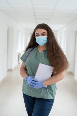 Kafkasyalı çekici kadın hemşire portresi. Klinik koridorunda üniforma ve steteskop giyiyor. Sağlık personeli