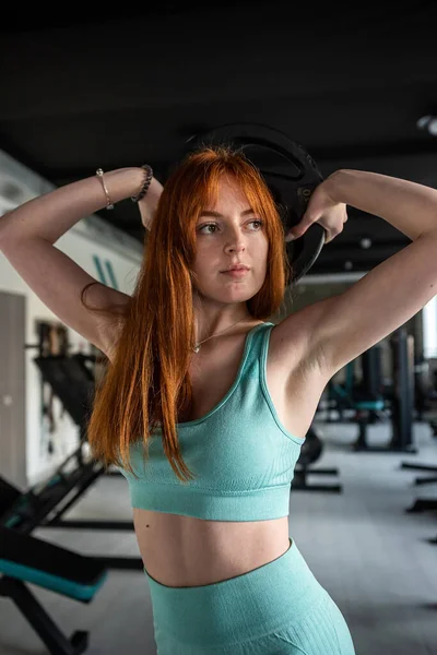 Strong red hair woman doing exercise with weight plate in the gym. Functional training, lifestyle