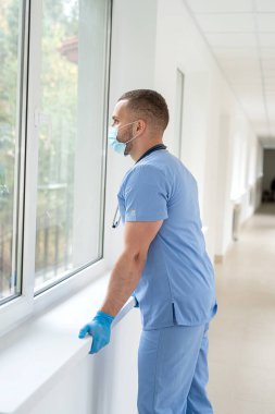 Klinikte mavi ceketli ve tıbbi maskeli beyaz bir erkek doktor. İşyeri