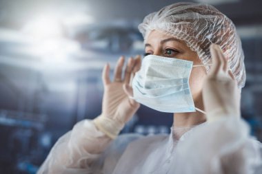  woman doctor in protective suit gloves putting surgical mask at clinic surgery before her work shift. Healthcare concept 