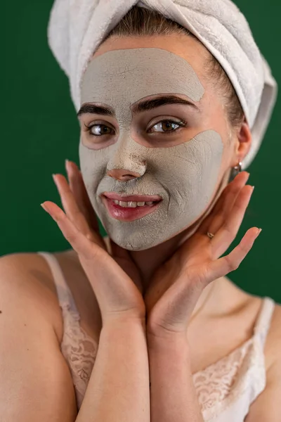 young woman getting green clay facial mask for skin care isolated on green. Spa anti aging procedures