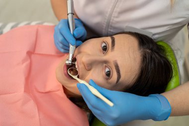 Diş kliniğinde dişlerini tedavi etmek için dişçi ve ağız aynası kullanan profesyonel bir dişçi. Sağlık hizmetleri