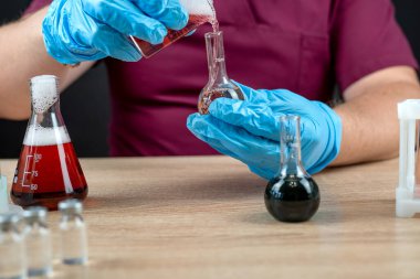 Bir adam laboratuarda test tüplerine sıvı karıştırıyor. Araştırma ve kimyasal deney.