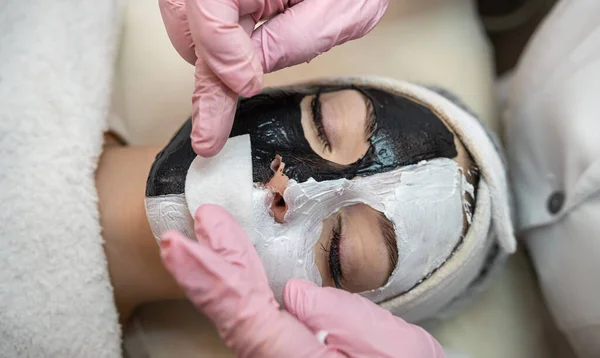 young woman with black and white clay cosmetic mask on half face lying a bad on spa salon. Skin care and treatment, lifestyle