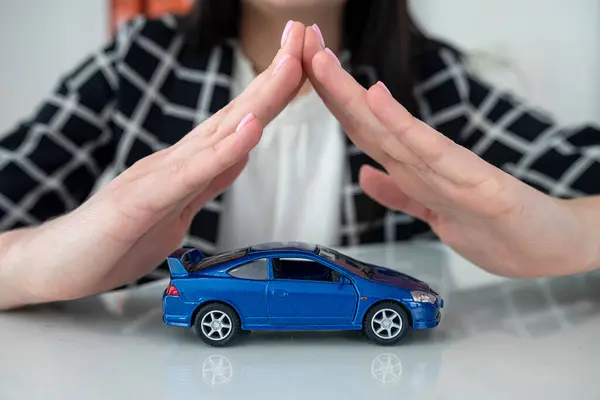 Small blue  toy car and female hand at office desk as insurance. Protection of automobile concept