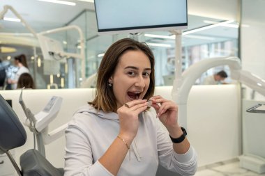 Close-up of a young Caucasian woman holding an invisible aligner that she wants to put on her teeth. Dental treatment concept.