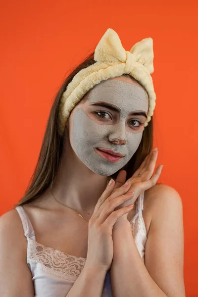 Portrait of young lady with green nourishing caly mask on face isolated on orange. Skin care healthcare cosmetic procedures