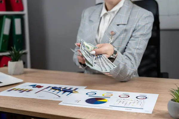 Female accountant count dollar paper money for payment salary and income at modern office, laptop and business graph and chart. Financial concept