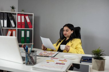 Dizüstü bilgisayarla çalışan güzel bir iş kadını ve özel ofisinde yeni planlanan finansal grafik verilerini belgeliyor. İşyeri