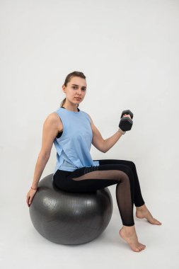 Güzel, genç bir kadın, rahat bir egzersiz yapıyor. Top ve halterlerle, halterlerin beyazını soyutluyor. Spor anlayışı