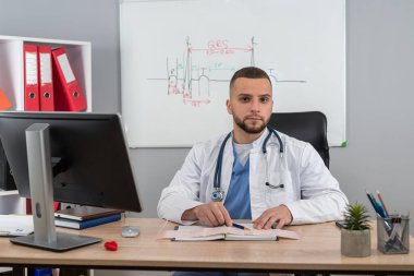 Genç doktor ya da pratisyen hekim hastane kliniğinde oturuyor. Sağlık raporuna yazma