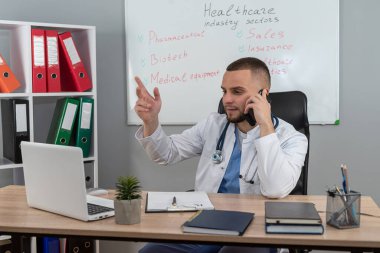 Modern klinikte masasında tek başına çalışan beyaz önlüklü ve steteskoplu doktor doktor portresi. Uzaklık hekimi kavramı