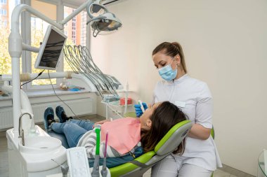 Kadın doktor diş hekiminin giriş kamerasını kullanıyor ve hastasının dişlerinin canlı görüntüsünü izliyor. Tedavideki son teknolojiler. Plaket ve kaplama önleme