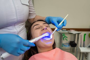 Diş hekimi, dişlerini beyazlatmak için mor ötesi lamba ve fotopolimer karışımı kullanıyor. Diş sağlığı ve sağlık hizmetleri kavramı