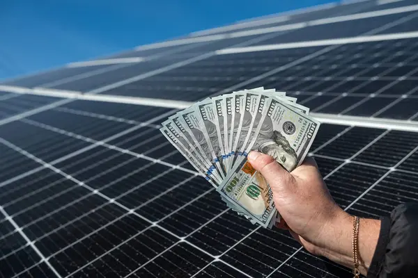 Saving money with solar energy and solar panels. Hand with dollars in front of panels. the concept of saving electricity