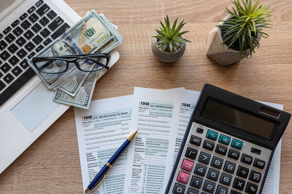 Налоговый сезон 1040 индивидуальная налоговая форма с ноутбуком и ручкой, долларовые купюры на рабочем столе. Крайний срок подачи документов 