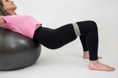  Sportif ve çekici bir kadın egzersiz yapıyor. Spor topu ve lastik bantla egzersiz yapıyor. Beyazın üstünde. Kaslarda işe yarıyor