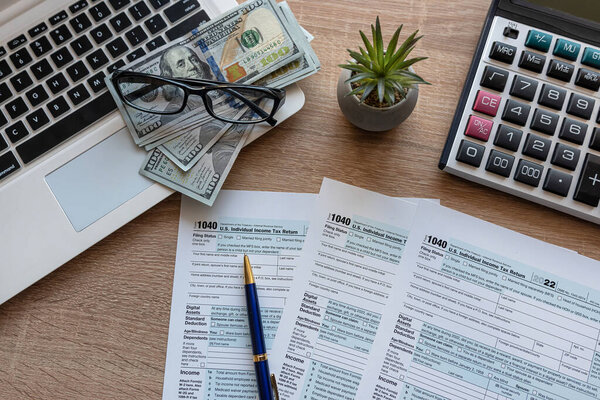 Tax Season 1040 individual tax form with with laptop and pen, dollar bills on office desk.  Deadline paperwork concept 