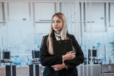 Beyaz kadın ofis müdürü. Ofiste görevli ve elinde pano var.. 