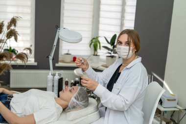 Kozmetik uzmanı, hasta kızın yüzünde gerekli yağı olan bir pipet tutuyor. Kaplıcadaki hastaya aromaterapi ve masaj kavramı