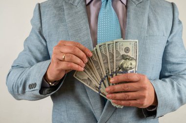 Takım elbiseli adam parayı sayıyor ve biz dolarları gri üzerine izole ediyoruz. Finans kavramı