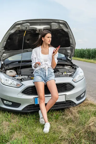 Kadın, yolda bozuk bir arabanın yanında telefon kulübesinde konuşuyor. Motor, sürmeye devam etmeyi imkansız kılıyor.