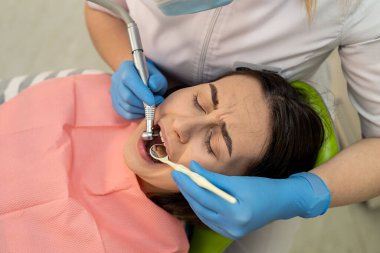 Diş hekimi kadın dişçi muayenehanesinde hastayı tedavi ederken diş matkabı ve ağız aynası kullanıyor. Stomatoloji ve sağlık hizmetleri kavramı 