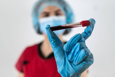 Kadın doktor kırmızı üniforma giyer, maske takar ve eldivenlerde beyaz üzerinde kan örneği olan test tüpü bulunur. ilaç covid19 salgını, aşı konsepti