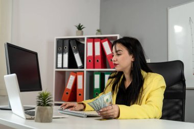 Genç Kafkasyalı iş kadını ofiste para ve dizüstü bilgisayarla dolar sayıyor. Ödeme maaşı ve gelir