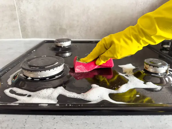 woman cleaning  sponge rag with white foam and detergent washing kitchen gas stove. House cleaning concept